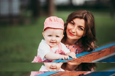 Young beautiful mother with a small child sitting on a bench in a park in pink clothesの写真素材