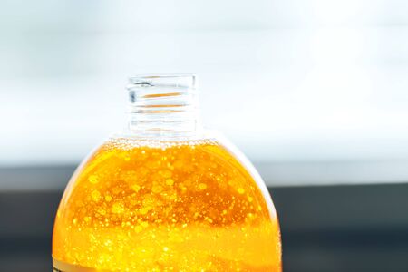 Liquid soap of orange color in a transparent bottle on a light background, liquid soap with bubblesの写真素材