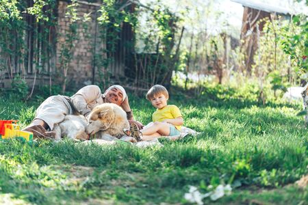Happy grandfather with grandchildren and a dog lie on a fresh lawn in the open air on a sunny dayの写真素材
