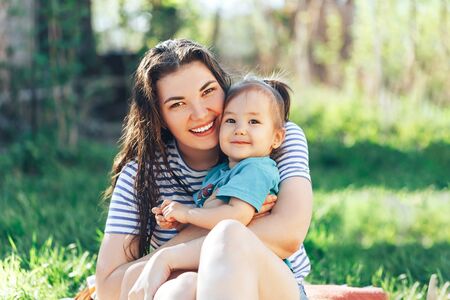 Young beautiful mother with daughter sit on an open-air lawn on a sunny dayの写真素材