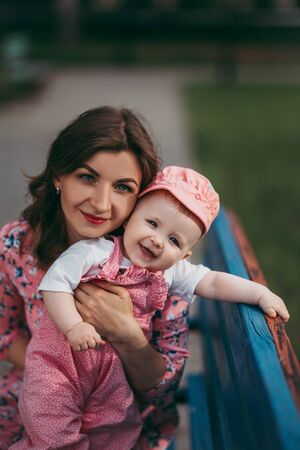 Young beautiful mother with a small child sitting on a bench in a park in pink clothesの写真素材