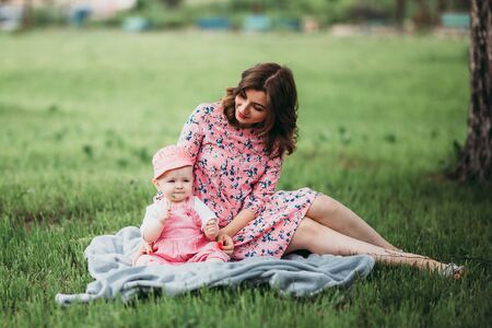 Young beautiful mother with small child have rest in the park on the lawn on warm day in pink clothes under the open skyの写真素材