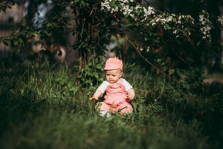 Little child sitting on lawn in park in pink clothes under the open skyの写真素材