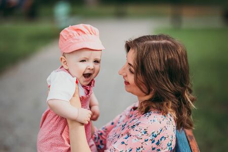 Young beautiful mother with a small child sitting on a bench in a park in pink clothesの写真素材