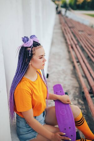 Young beautiful girl holding a skateboard in her hand in a yellow T-shirt and yellow socks in the open air, top view.の写真素材