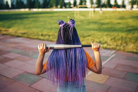 Young beautiful girl holding a baseball bat in a yellow open-air t-shirt in a sports stadium.の写真素材