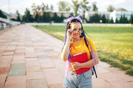 Young beautiful girl holding a red folder in her hand in a yellow T-shirt walking in the open air at a sports stadiumの写真素材
