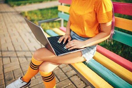 Young beautiful girl holding a laptop in a yellow t-shirt sitting on a bench in the open airの写真素材