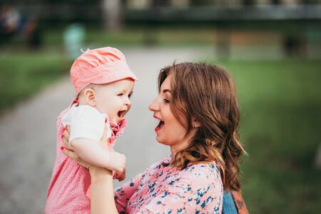 Young beautiful mother with a small child sitting on a bench in a park in pink clothes.の写真素材