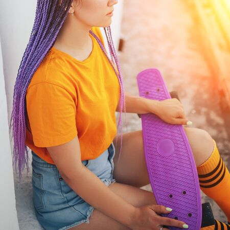 Young beautiful girl holding a skateboard in her hand in a yellow T-shirt and yellow socks in the open air, top view.の写真素材