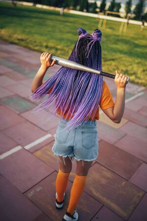 Young beautiful girl holding a baseball bat in a yellow open-air t-shirt in a sports stadium.の写真素材