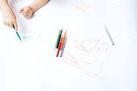 Little child draws on white paper with colored felt-tip pens, teaching children to draw.