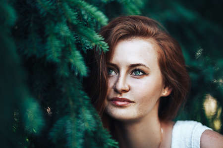 Young beautiful girl with red hair and with freckles on her face, red-haired girl on a background of the Christmas tree.の写真素材