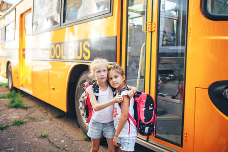 Schoolgirls with backpacks on the background of a school bus, back to school