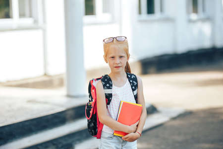 Schoolgirl with a backpack and glasses holding a book in her hands, back to school.の写真素材