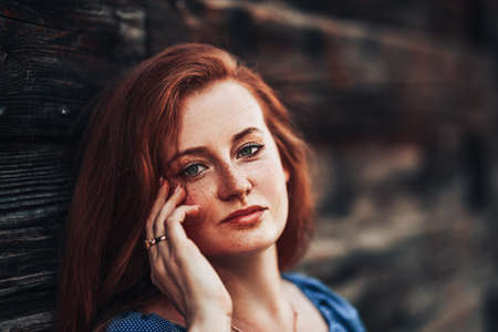 Beautiful red-haired girl on a background of a wooden wall in a blue dress, spring time, natural beauty.の写真素材