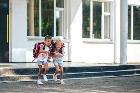 Two schoolgirls holding each other's hands flee from school, back to school, primary education of children.の写真素材