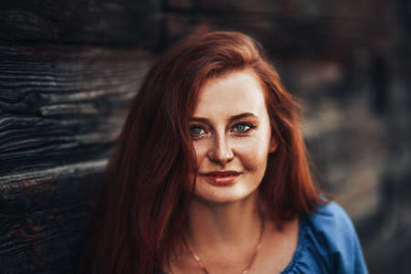 Beautiful red-haired girl on a background of a wooden wall in a blue dress, spring time, natural beauty.の写真素材