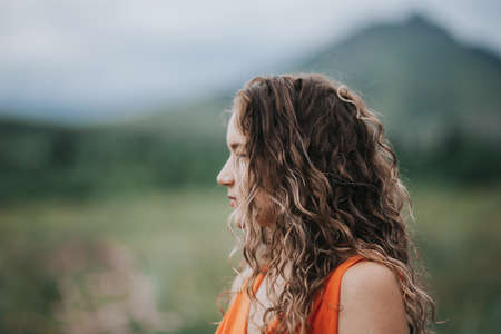 Close-up photo of a girl in an orange dress against a background of mountains, portrait photo of a young girl.の写真素材