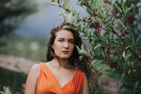 Girl in an orange dress on a background of a tree with fruits, portrait photo of a young girl.の写真素材