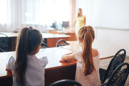 Two little schoolgirls sit at a desk in a school class and carefully listen to the teacher.の写真素材