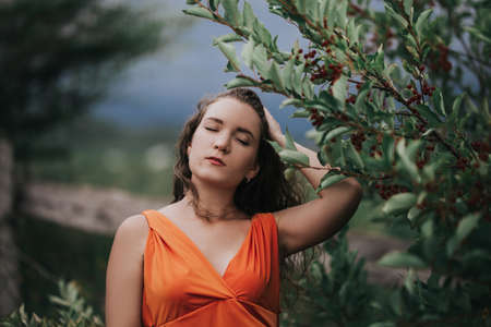 Girl in an orange dress on a background of a tree with fruits, portrait photo of a young girl.の写真素材