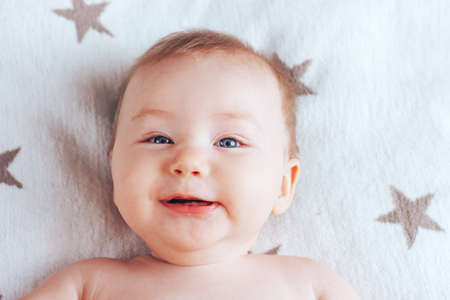 Photo of a smiling baby, a newborn baby with blue eyes and blond hair lying on a light blanket with brown starsの写真素材