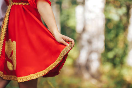 Girl in national Russian clothes of red color and golden ornaments on a background of green grass.の写真素材