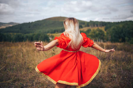 Young blonde girl dressed in national Russian clothes of red color outdoors in the field.の写真素材