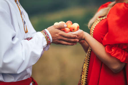 A guy and a girl dressed in national Russian clothes holding a plate of apples.の写真素材