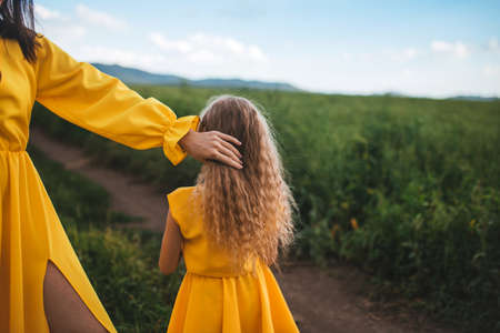 Mom and daughter in yellow dresses standing in the open air on a background of grass.の写真素材