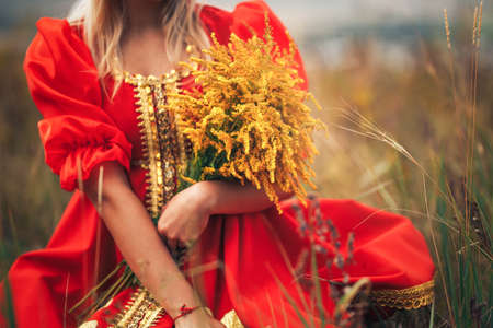 A girl in national Russian clothes holding a beautiful bouquet of yellow flowers in her hand. Art grain and noise on photoの写真素材