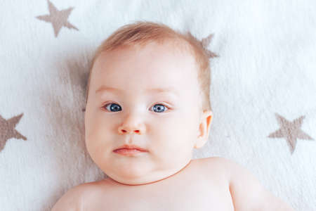 A photo of an emotionless baby, a newborn baby with blue eyes and blond hair lying on a light blanket with brown stars.の写真素材