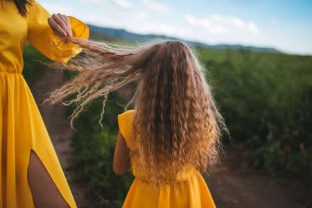 Mom and daughter in yellow dresses standing in the open air on a background of grass.の写真素材