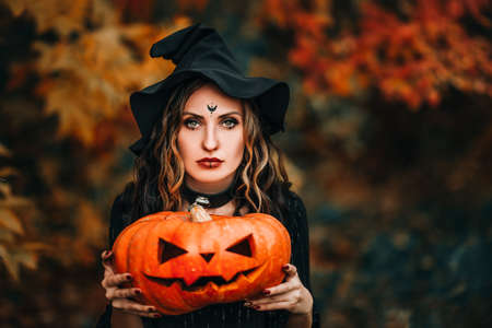 Woman in halloween witch costume holding a large pumpkin with carved face.
