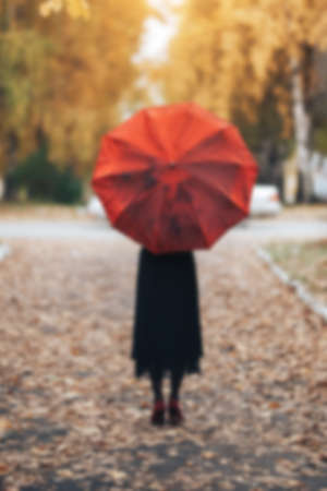 Woman walking in the park in autumn weather under a red umbrella. blurred photo, unfocusedの写真素材