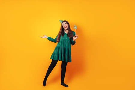 Beautiful woman celebrates her birthday on a yellow background in green dress and on her head festive cap holds the number 28 in her hand.の写真素材