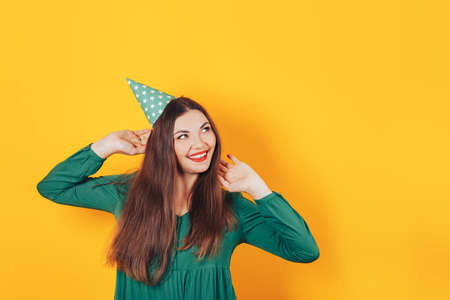 Happy beautiful girl in a green dress on a yellow background, smile. festive cap on her head.の写真素材