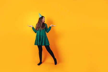 Happy beautiful girl in a green dress on a yellow background, smile. festive cap on her head.の写真素材