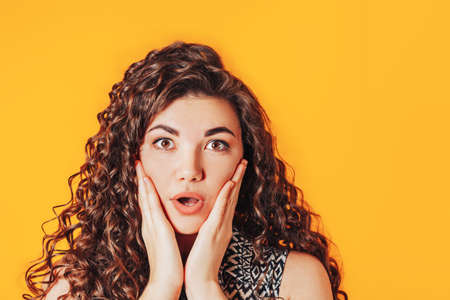 Beautiful woman with curly hair posing at camera on yellow background.の写真素材