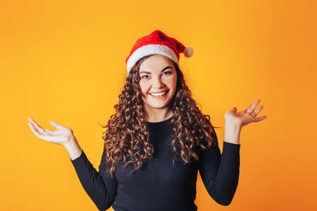 Beautiful woman in a black sweater and a red christmas hat on her head on a yellow backgroundの写真素材