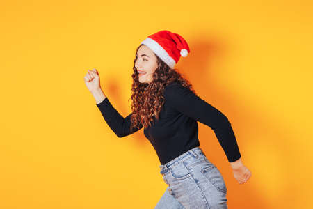 Beautiful woman in a black sweater and a red christmas hat on her head on a yellow backgroundの写真素材