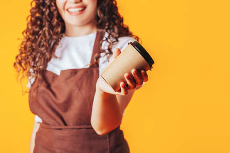 Young woman dressed in a brown uniform holding a cup of coffee on a yellow background.の写真素材