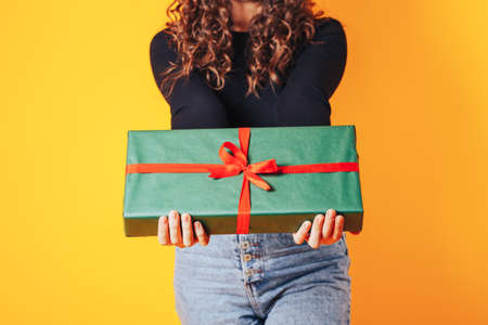 Woman holding large box in her hands. Gift in green packaging with red ribbon and red bow. Gift for woman for holiday or special occasion.の写真素材