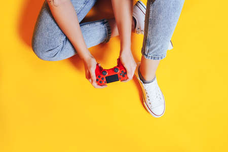 Woman holding gamepad in her hands in against of a yellow background. Promotion of women's esports. Advertising of esports equipment. Flat lay. Place for text.の写真素材