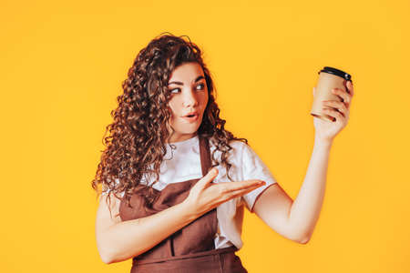Woman holding a cup of hot coffee in her hands. Surprised woman points with hand to disposable cup. Coffee shop advertisement. Place for your text.の写真素材