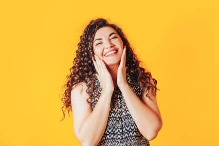 Young beautiful woman shows emotion pleasure. Beautiful curly hair. Advertising of a beauty salon and dentistry. Place for your text.の写真素材