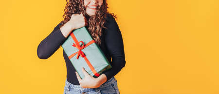 Woman holding large box in her hands. Gift in green packaging with red ribbon and red bow. Gift for...