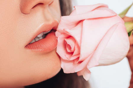 Close-up of woman's face on white background. The woman's lips have a pink rose.の写真素材