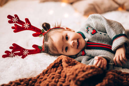 Little girl lying on a big bed. The child has antlers on his head. Christmas mood.の写真素材